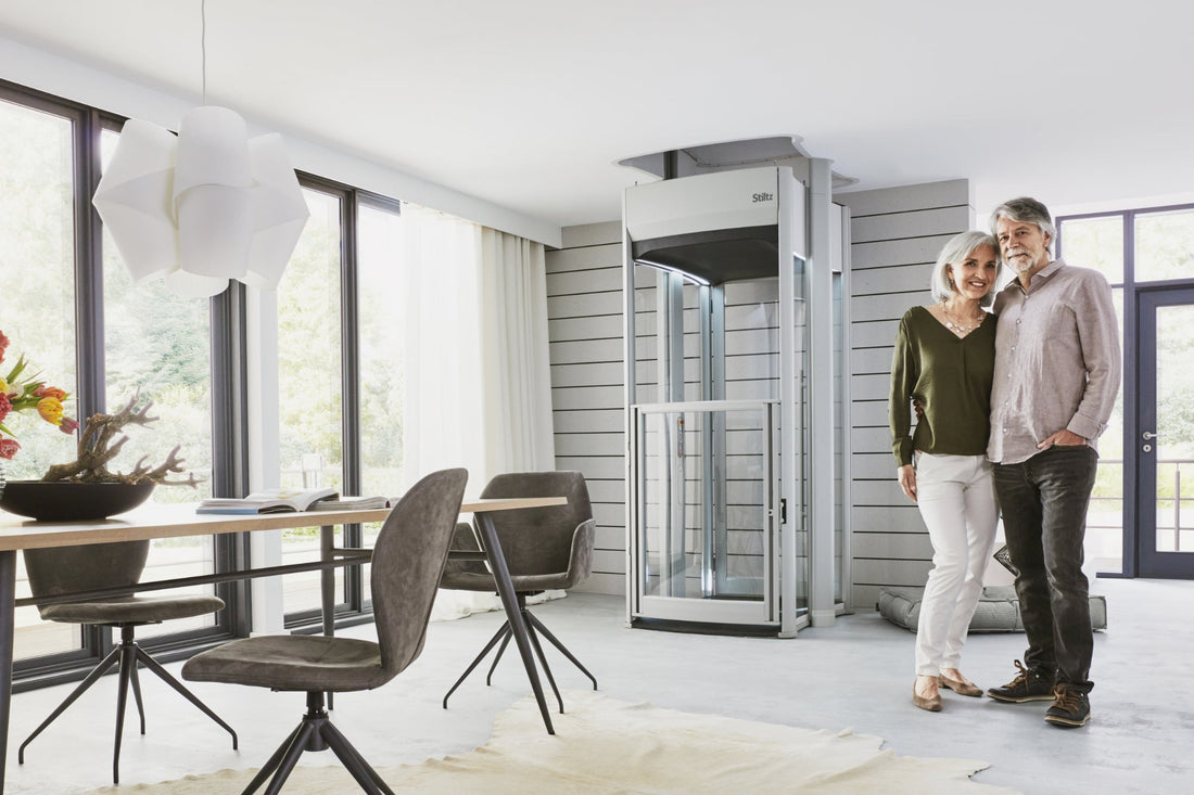 Couple standing beside a glass home lift in an open plan living and dining area