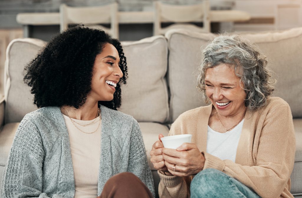 Two women smiling and drinking tea on the couch together