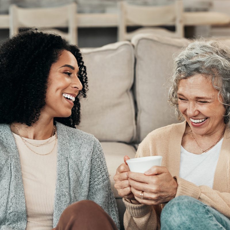 Two women smiling and drinking tea on the couch together