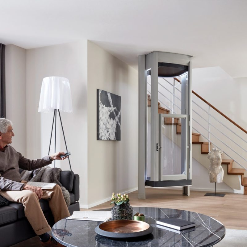 Elderly Man sitting down in living room with a home lift in the background