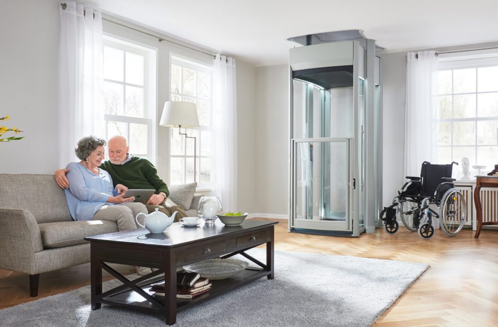 Senior Couple looking at iPad sitting down in a living room. Home lift in the back corner.