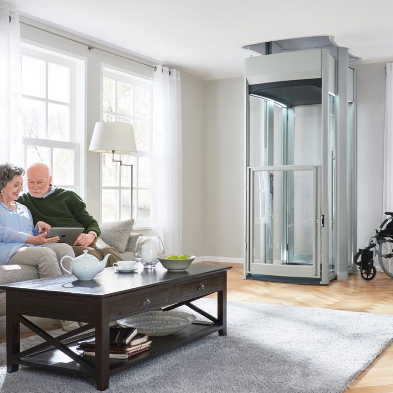 Senior Couple looking at iPad sitting down in a living room. Home lift in the back corner.
