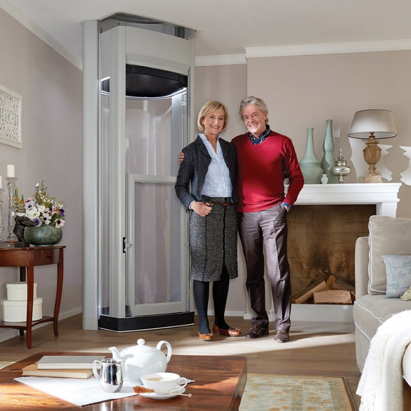 Elderly Couple Smiling with a home lift in living room.